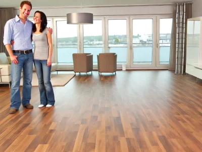 DALL·E-2024-06-14-11.45.44-A-happy-couple-standing-in-their-modern-living-room-admiring-their-newly-installed-wood-floors.-The-room-is-bright-and-spacious-with-large-windows-l.webp